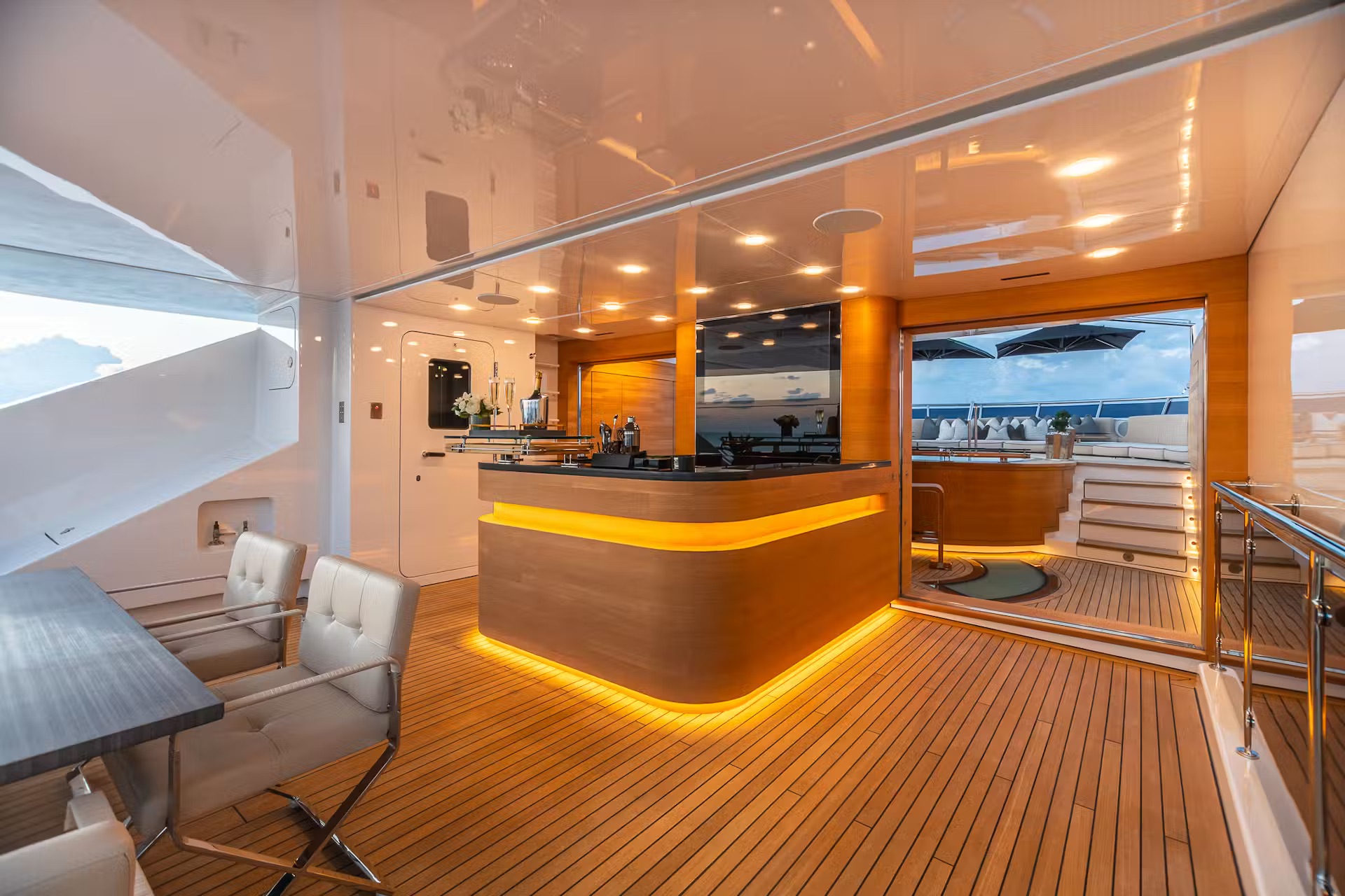 Elegant onboard bar lounge at dusk with warm ambient lighting, wood paneling, guests enjoying champagne at high-top table.