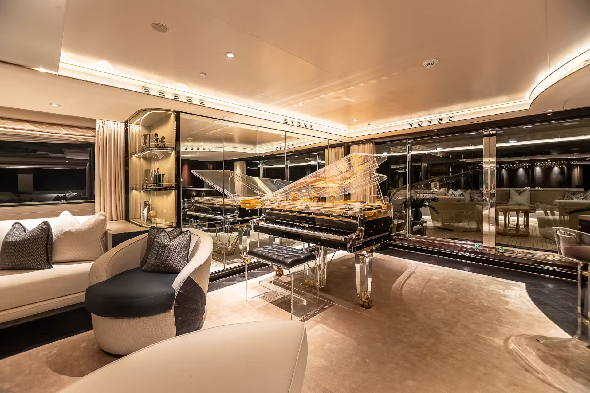 Main saloon with cream curved seating, sculptural accents, grand piano and floor-to-ceiling sea views.
