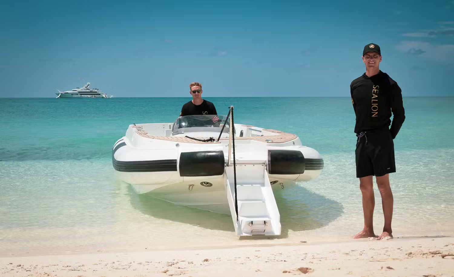 Tender boat and crew members beached in turquoise water with superyacht anchored offshore