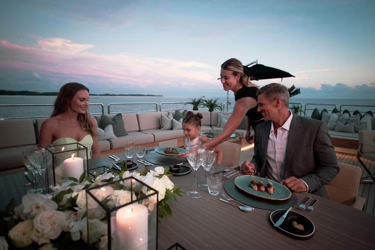 Family dining at sunset on the upper deck with ambient candlelight and ocean backdrop